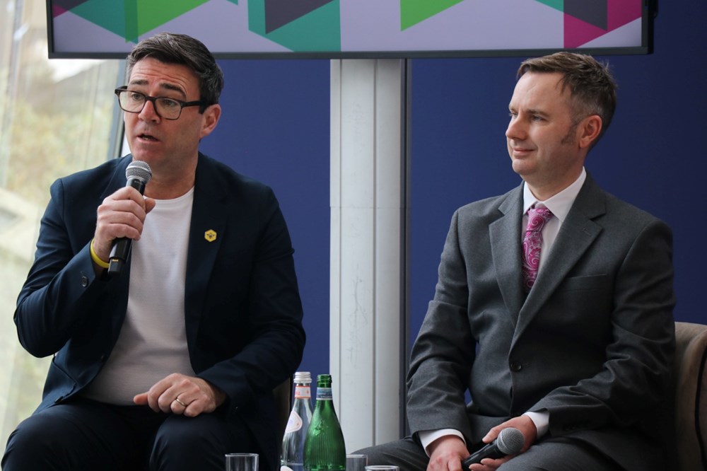 Andy Burnham, holding a microphone and speaking, sits alongside Cllr Tom Ross