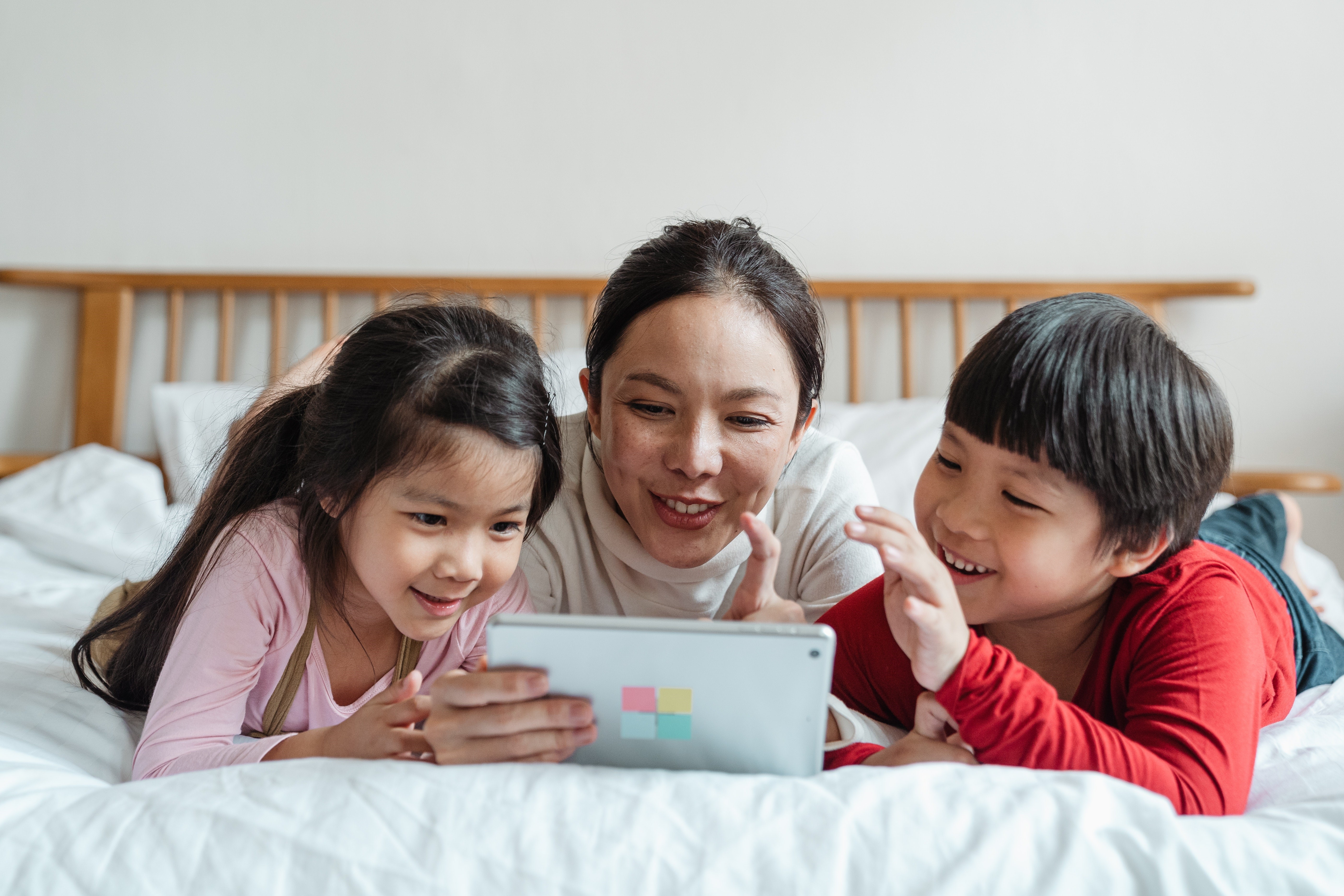 Woman and two children looking at tablet device while lying on bed