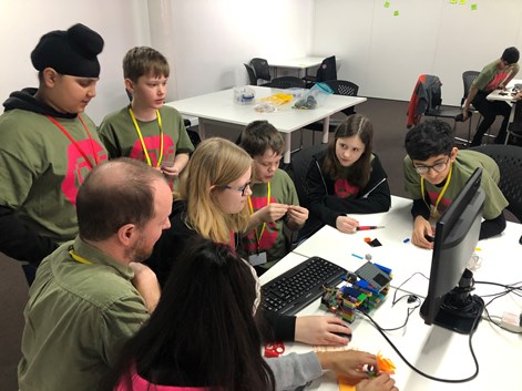 A group of young people all huddled around a computer with a lego robot in front of them