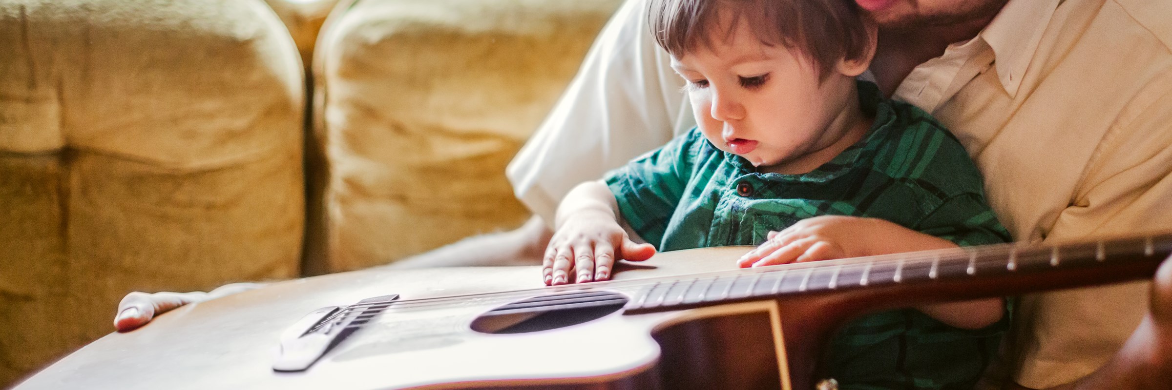 An adult with a child on their lap both playing with a guitar