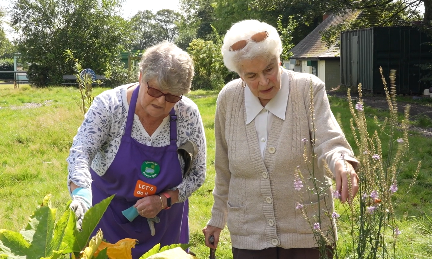 Two older people in a park garden looking at flowers.