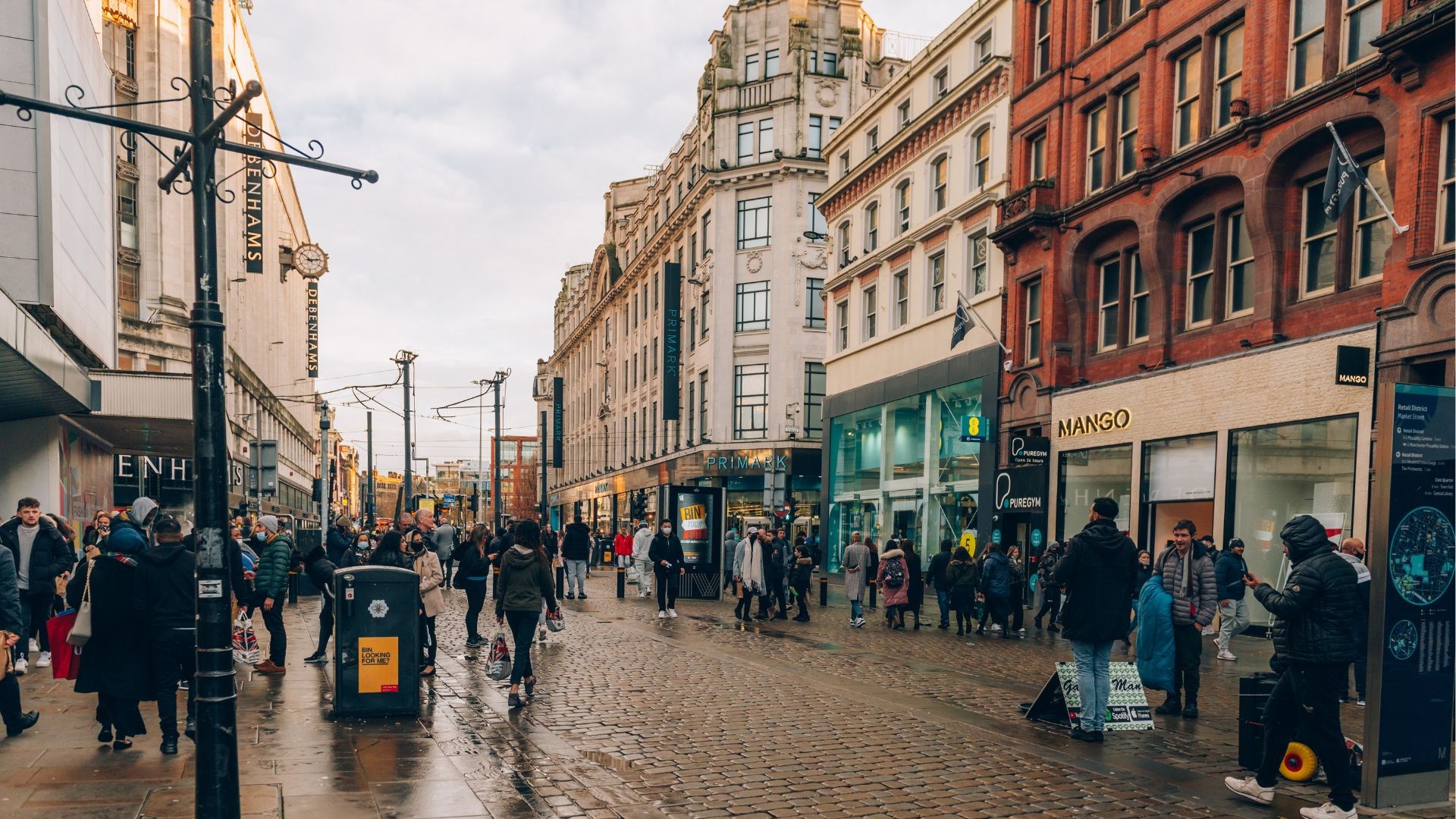 A busy city street  in Manchester with people walking and standing on the pavement