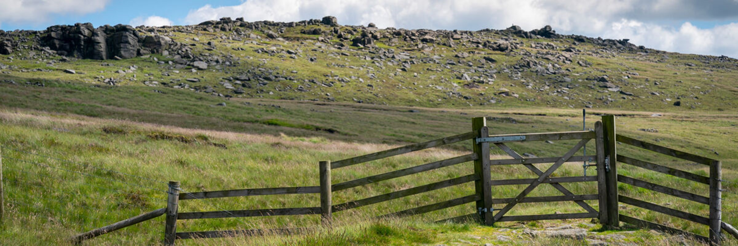 South Pennine Moors. Green grass over the hills with a wooden gate in the foreground