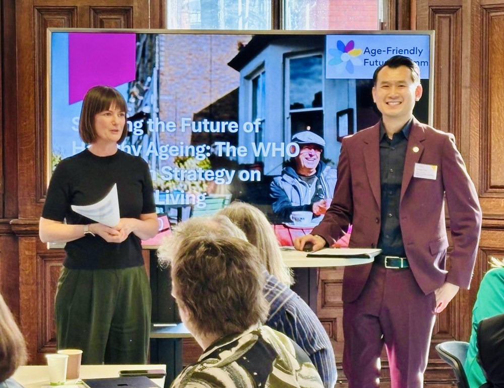 Two people standing in front of a large screen presenting to a group