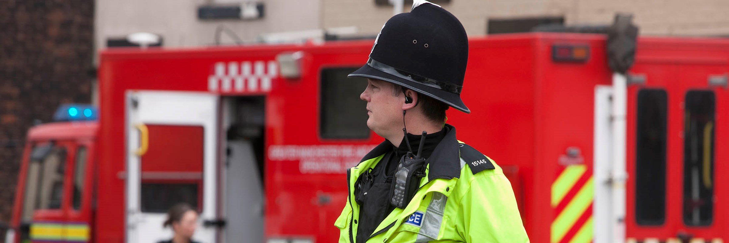 Police officer in high-vis coat stands in front of fire engine