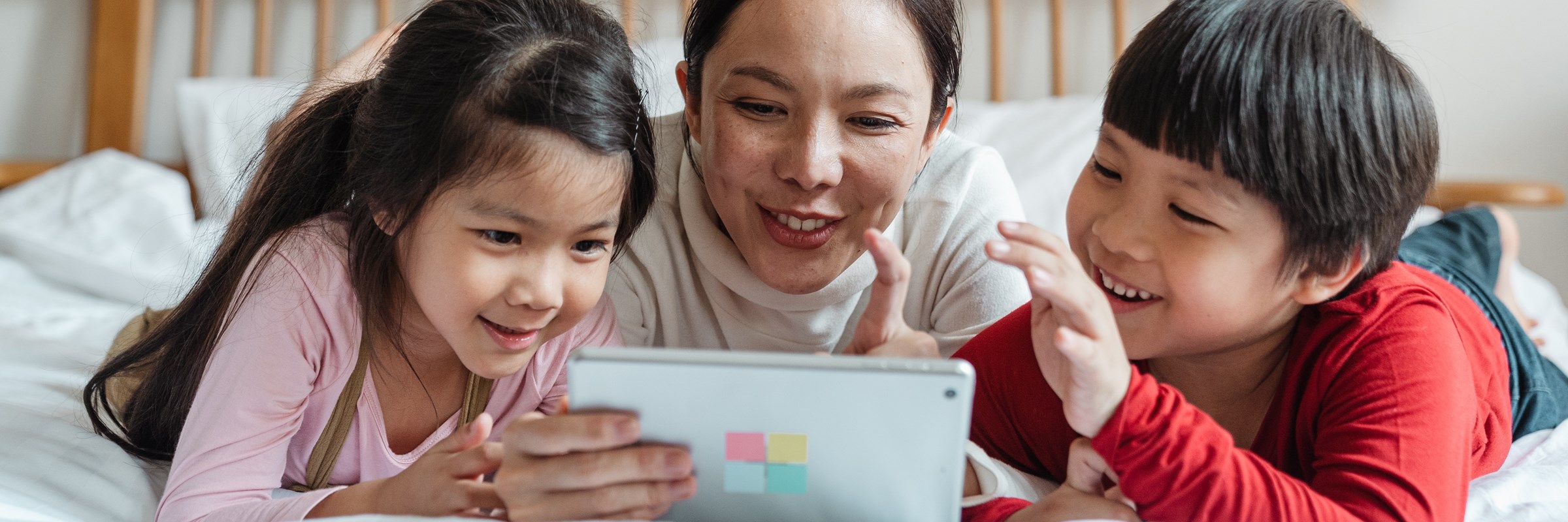 Woman and two children looking at tablet device while lying on bed