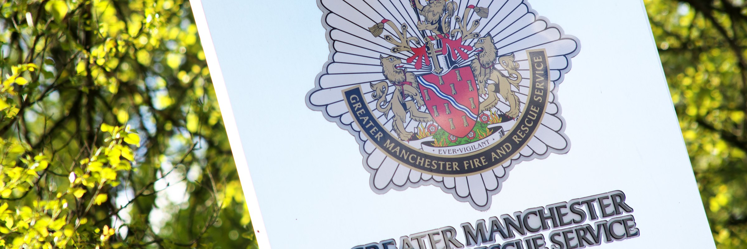 Greater Manchester Fire and Rescue Service sign with bright green leaves on a tree just behind it