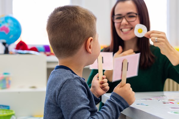 A teacher smiling and teaching a child showing a cut out picture of a sun, the child is holding two signs