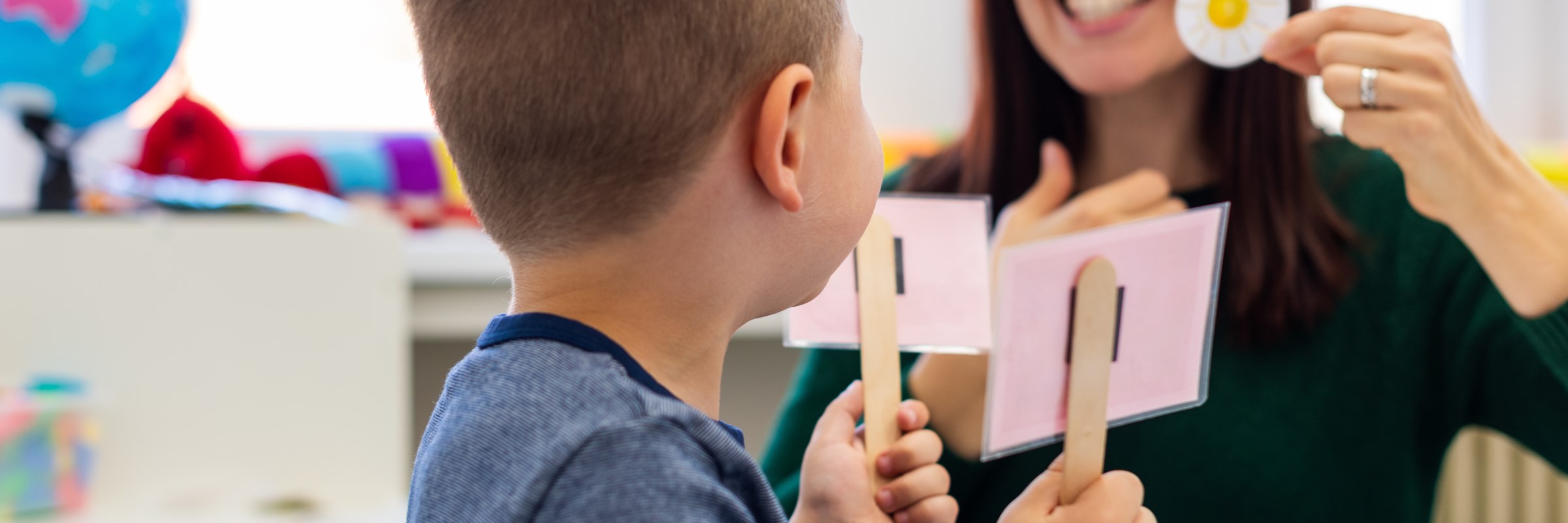 A teacher smiling and teaching a child showing a cut out picture of a sun, the child is holding two signs