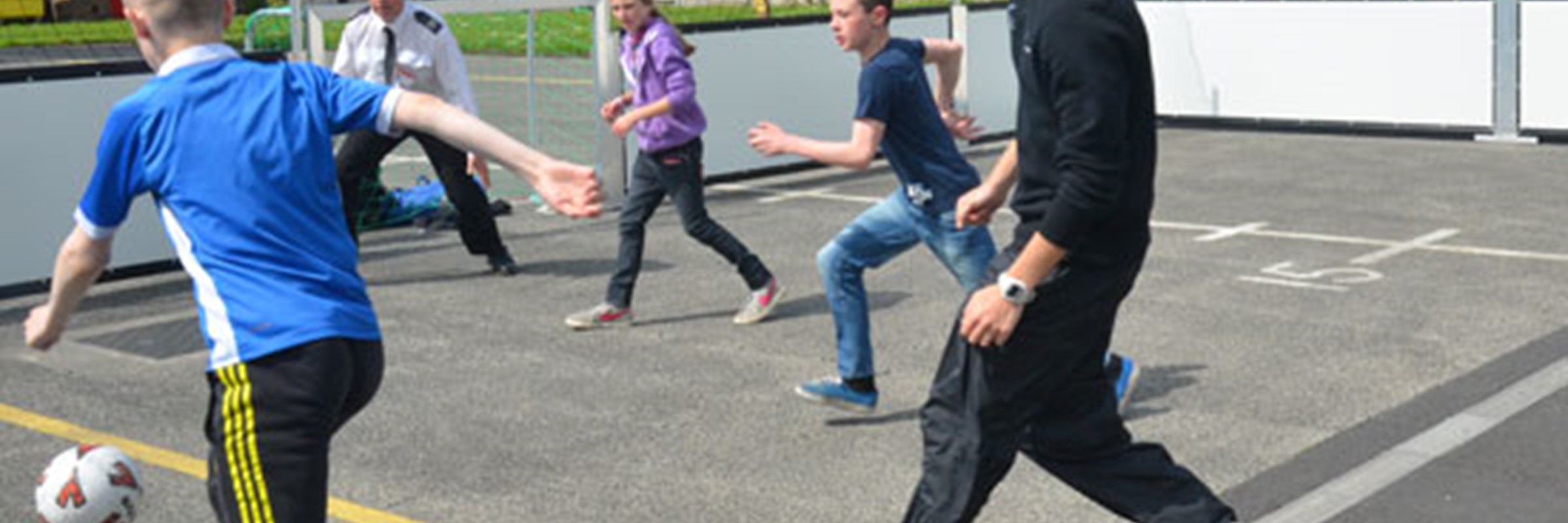 Five people playing a ball game which is taking place on an outdoor court. A house is in the background.