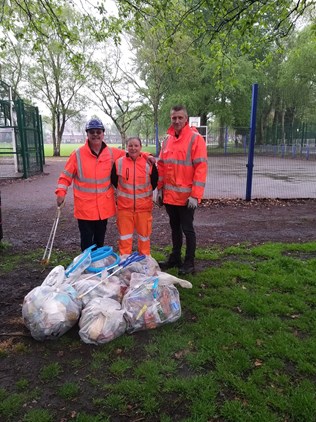 Three Suez staff wearing hi-viz and holding litter pickers stand in front of six bags of rubbish