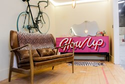 One of the display pods at the Renew Hub, featuring a vintage armchair with leopard print throw, bicycle hanging from the wall, and a pink sideboard with the words 'glow up' painted on the front