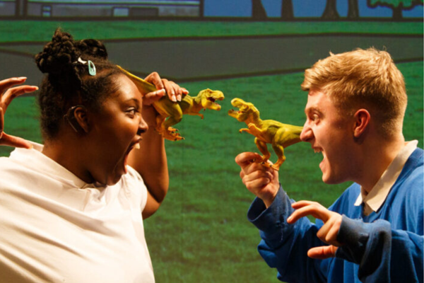 Two people on stage holding toy dinosaurs and growling at one another