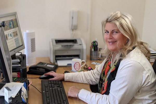Ladderstore MD Gail Hounslea sits at a desk in front of a keyboard and monitor - she has a light jacket, coloured scarf and blonde hair