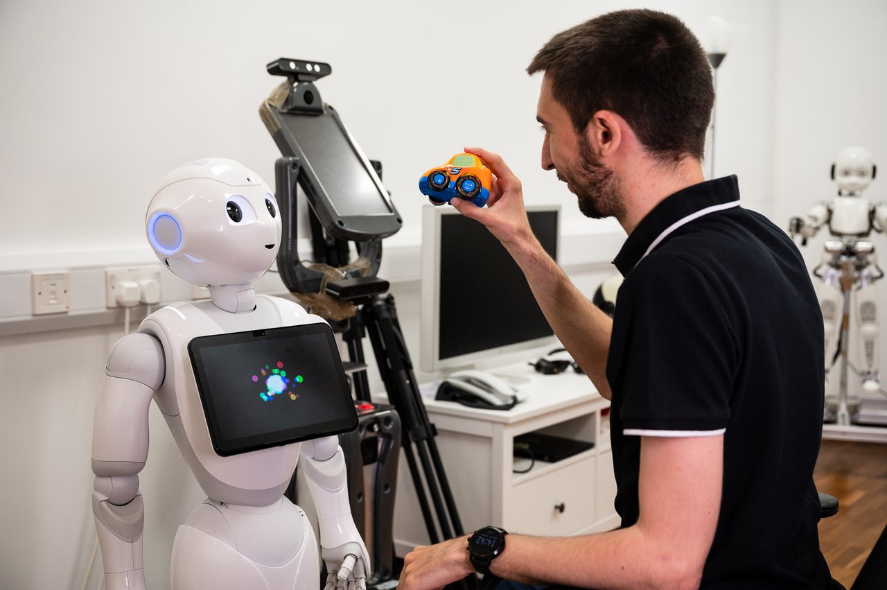 Person holding a toy car up to a robot