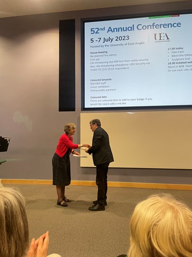 Man in suit shaking woman's hand in front of a projector screen.