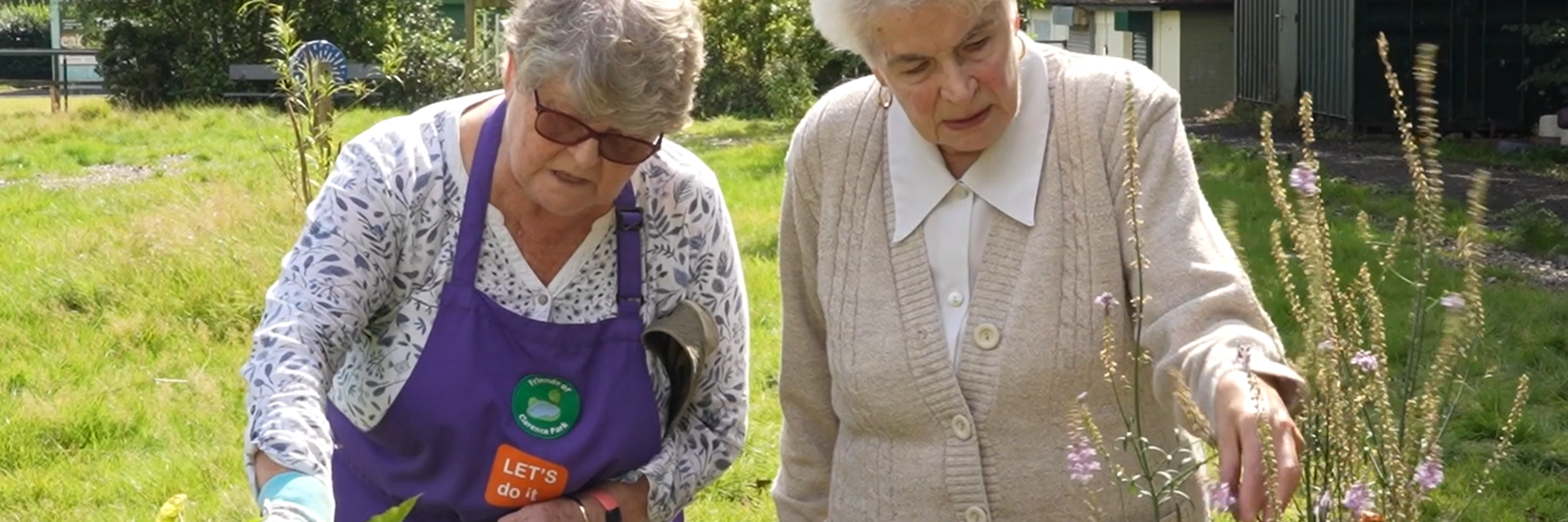 Two older people in a park garden looking at flowers.