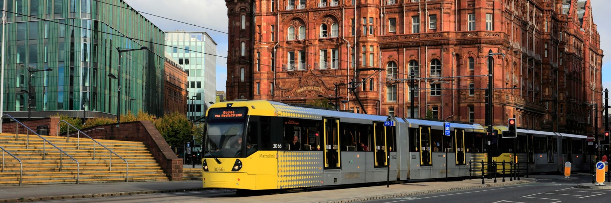 A yellow tram on the tracks in front of a large building in Manchester