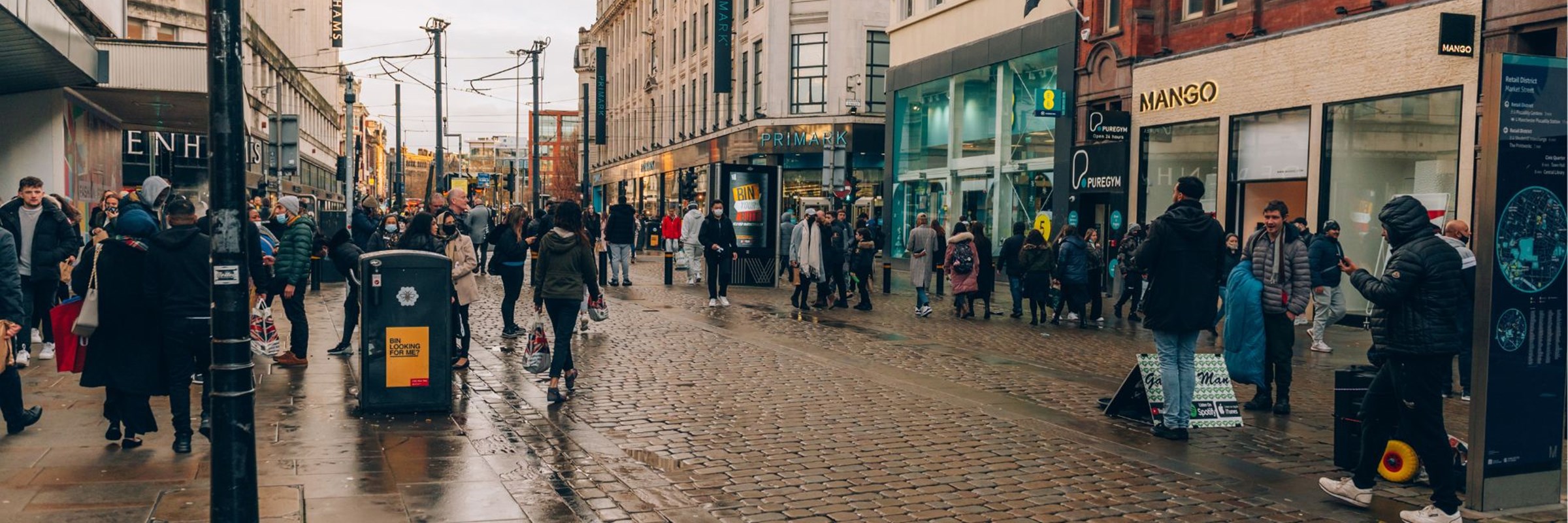 A busy city street in Manchester with people walking and standing on the pavement