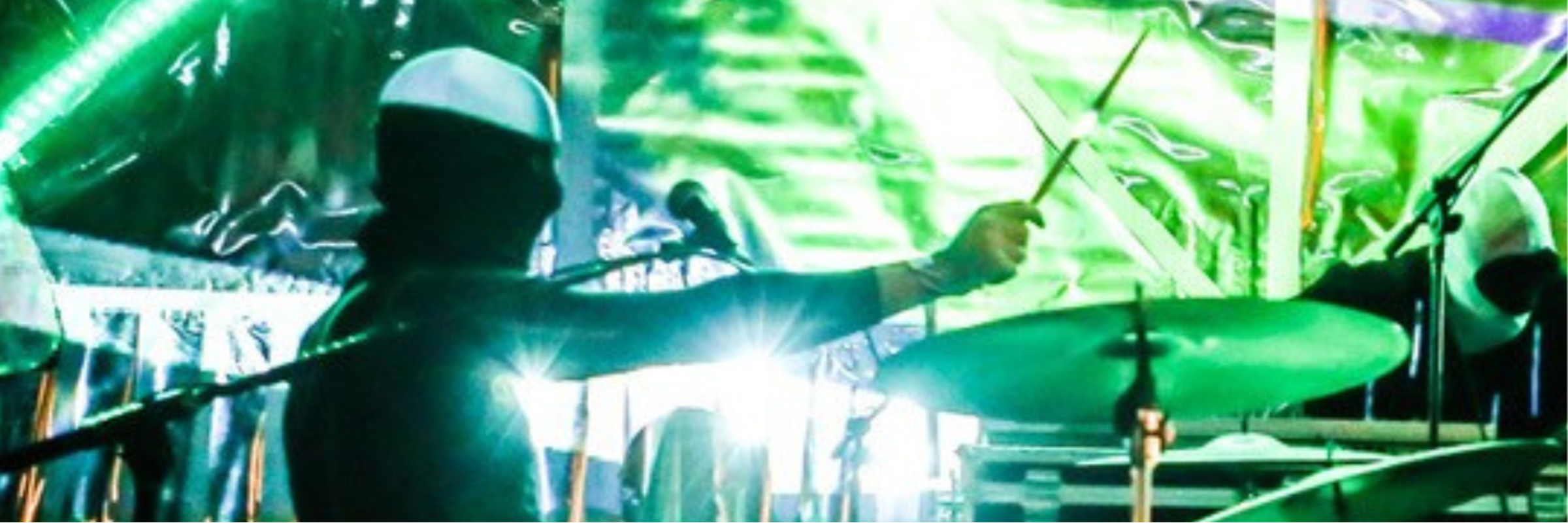 A person playing the drums surrounded by green lasers and lights