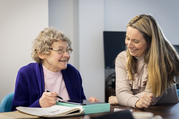 Image of older woman being supported by a younger woman to use a tablet device.