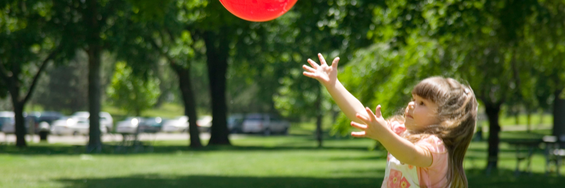Toddler aged girl playing with a red ball in a park