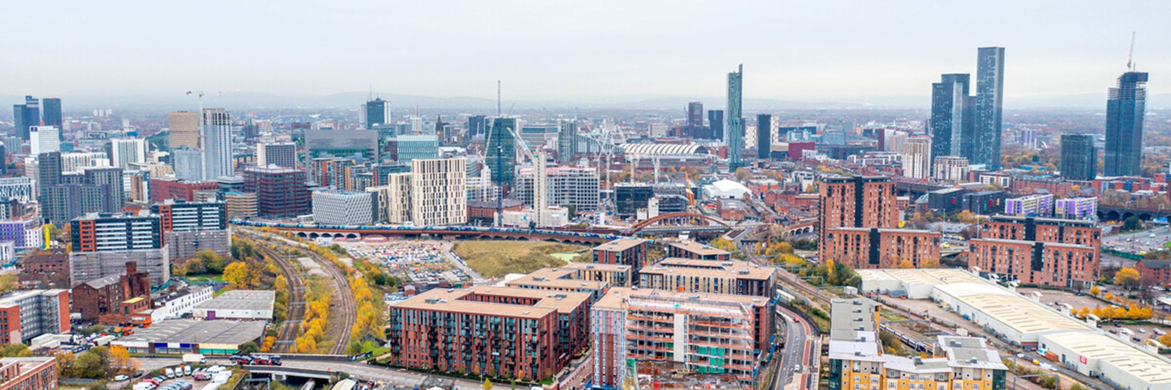 Aerial view of central Manchester, UK, featuring modern high-rise buildings, construction sites, and railway lines.