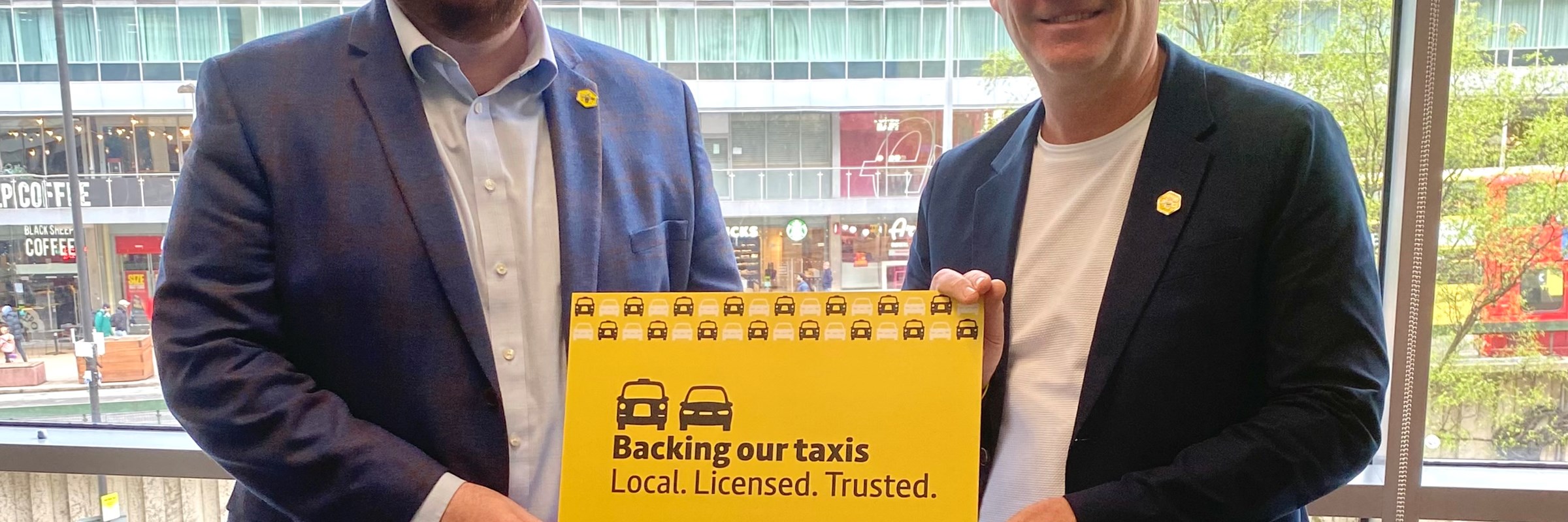 Andy Burnham and Cllr Eamonn O'Brien stand together holding a card that reads "Backing our taxis."