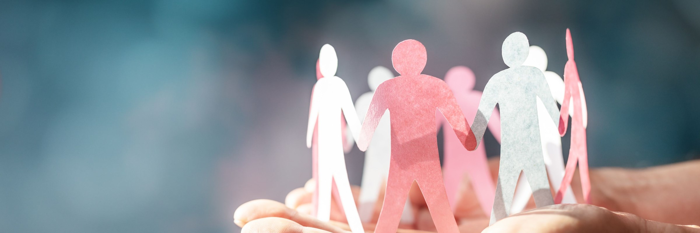 A pair of hands facing palm upright holding a paper chain of people figures holding hands in pink and white paper.
