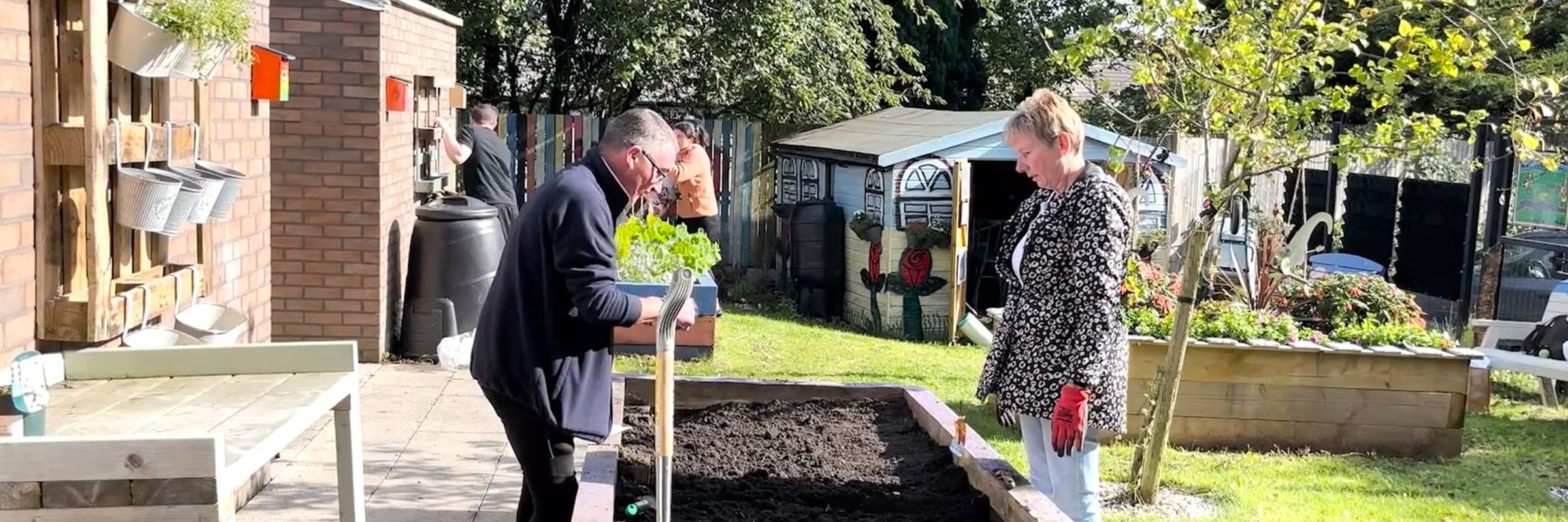 Two people with gardening gloves on planting seeds in a bed.